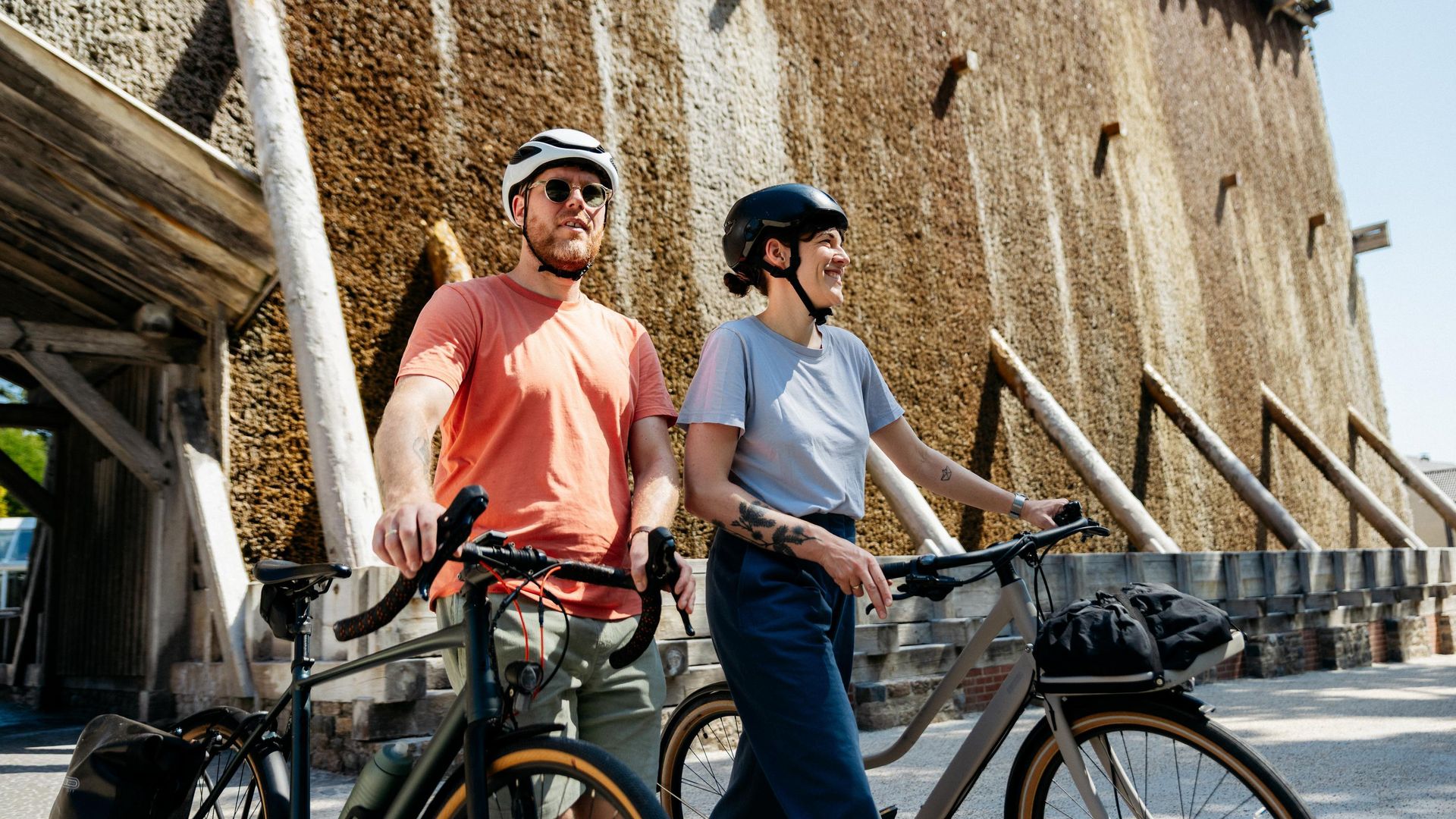 Zwei Radfahrer mit Helmen neben Fahrrädern vor einer beeindruckenden Gradierwerkstruktur.