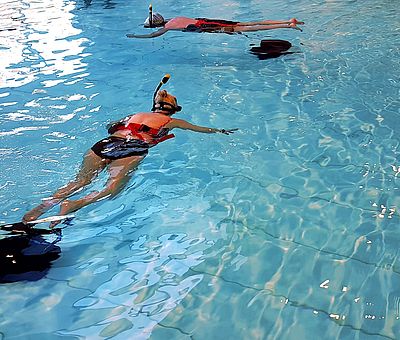 Auf diesem Bild bekommt man einen Ausschnitt vom VR-Schnorcheln im Nettebad in Osnabrück zu sehen. Im Wasser schwimmen zwei Frauen und sind dabei zu schnorcheln. Währenddessen tragen sie VR-Brillen.