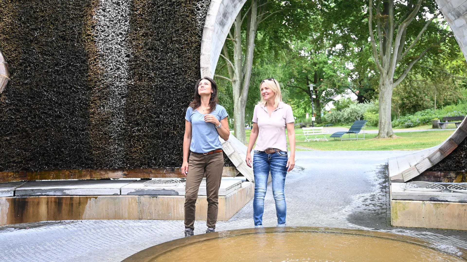 Zwei Frauen spazieren lächelnd durch einen Gradierwerk-Pavillon im Park.