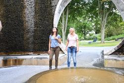 Zwei Frauen spazieren lächelnd durch einen Gradierwerk-Pavillon im Park.