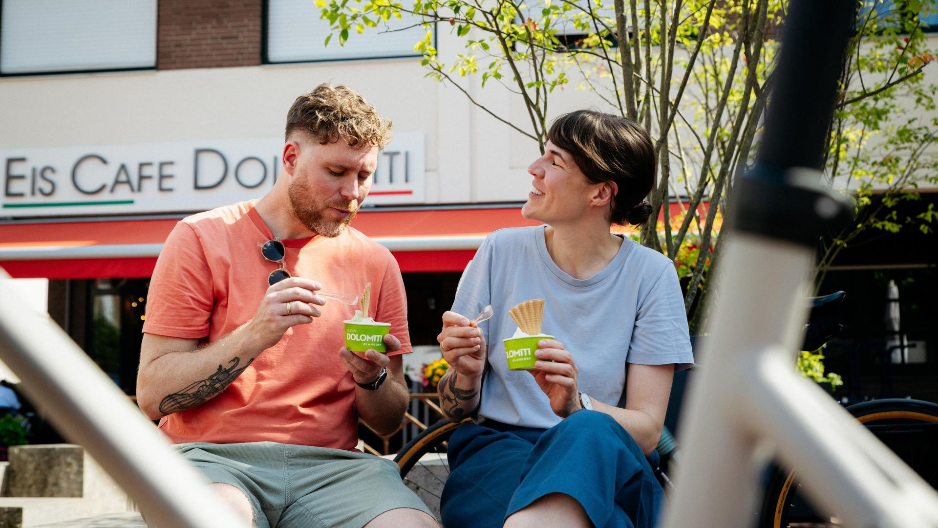 Zwei Personen genießen Eis vor einem Café bei sonnigem Wetter.