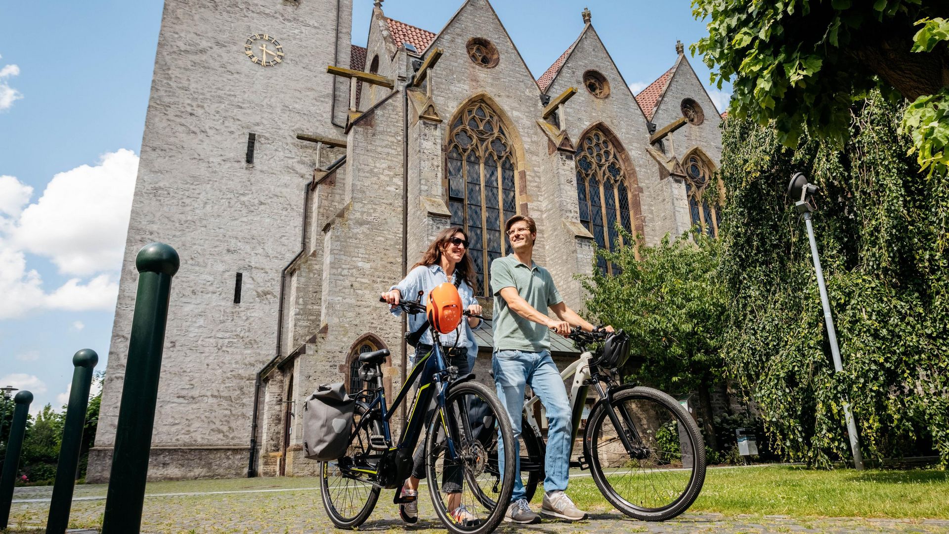 Zwei Menschen mit Fahrrädern vor einer historischen Kirche mit gotischen Fenstern.