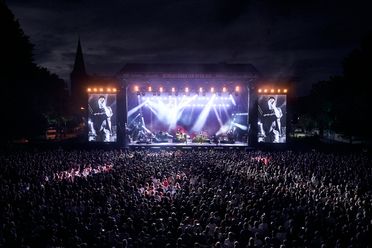 Eine energiegeladene Open-Air-Konzertszene in Osnabrück: Vor einer beeindruckend beleuchteten Bühne feiert ein großes Publikum die Live-Performance der Künstler. Die Bühne ist mit intensiven Lichtshows und einer großen Leinwand ausgestattet, auf der ein Sänger in Aktion zu sehen ist. Diese dynamische Aufnahme vermittelt die lebhafte Atmosphäre und die Begeisterung, die Osnabrücks Veranstaltungskultur prägen.