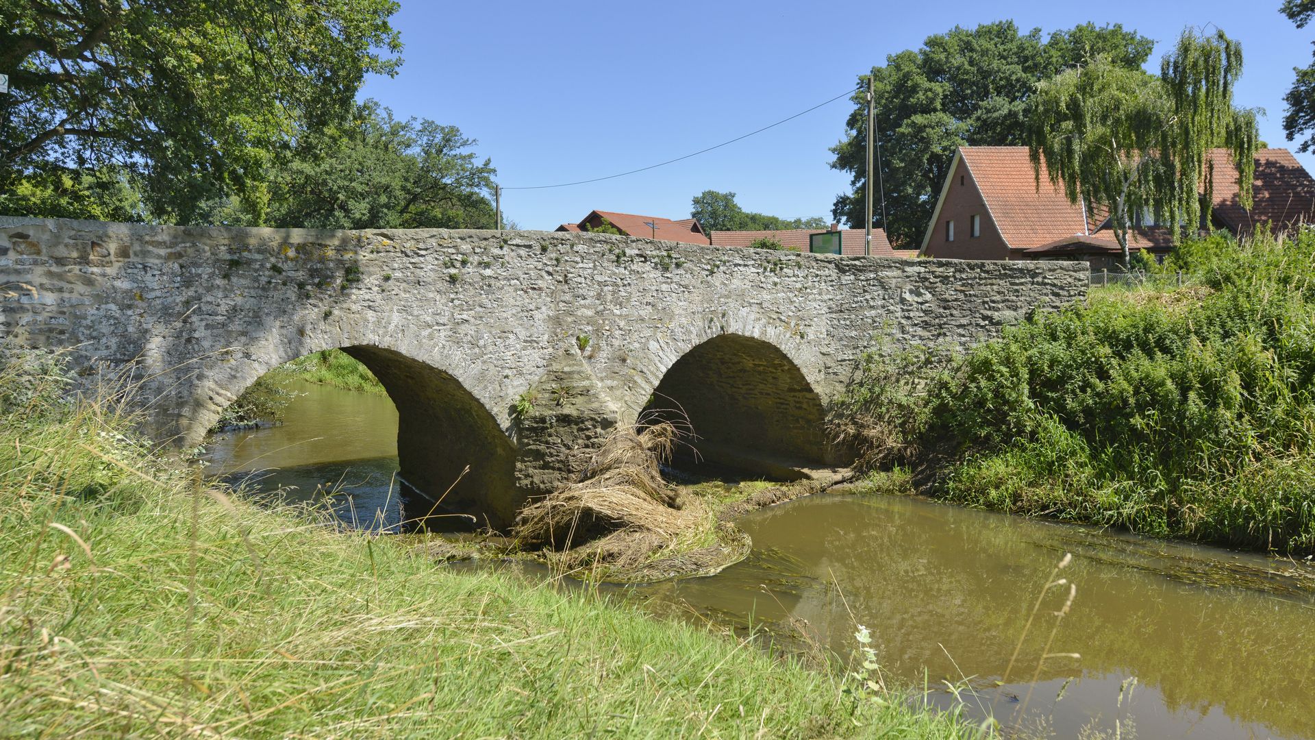 Historische Römerbrücke über die Hunte, umgeben von Wiesen und naturnaher Flusslandschaft.