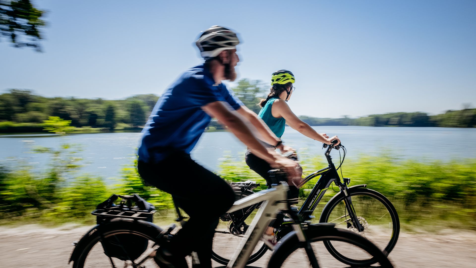 Zwei Radfahrer genießen eine Fahrt entlang eines ruhigen Sees an einem sonnigen Tag.