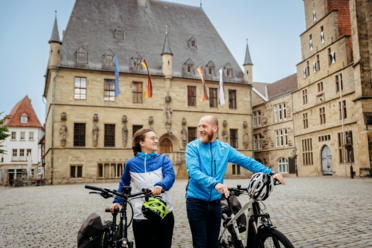 Zwei Personen mit Fahrrädern vor einem historischen Gebäude in einer Altstadt.