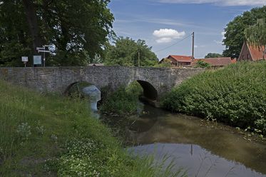 Historische Römerbrücke über die Hunte, eingebettet in eine ruhige Fluss- und Wiesenlandschaft.