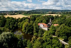 Luftaufnahme eines Herrenhauses und einer Kirche umgeben von üppigen Bäumen und einem Teich.