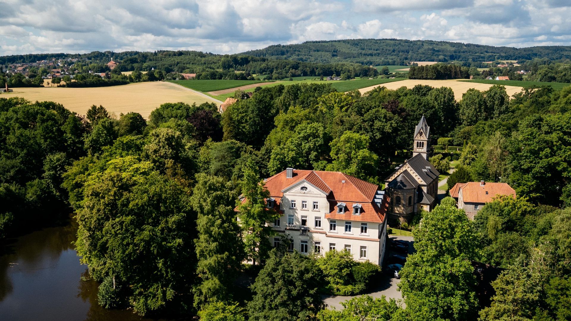 Historisches Gutshaus inmitten von Wald und Wiesen, daneben eine kleine Kapelle.