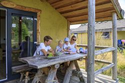 Familie sitzt entspannt an einem Holztisch auf einer überdachten Terrasse, genießend Zeit im Freien.
