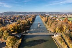 Brücke über einen herbstlichen Fluss mit Frachtschiff, umgeben von buntem Laub.