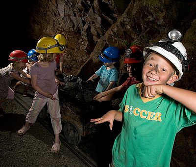 Kinder als Museumsbesucher schieben eine Lore mit Kohle im Stollen vom Museum Industriekultur in Osnabrück.