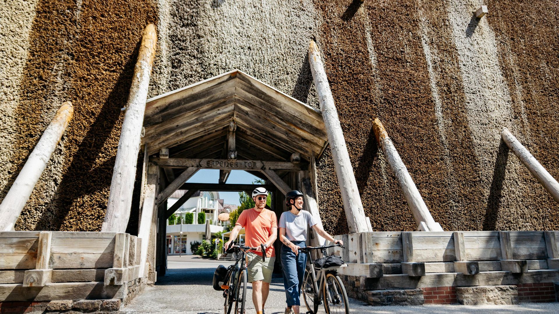 Zwei Radfahrer stehen vor einem monumentalen Gradierwerk aus Holz und Reisig.