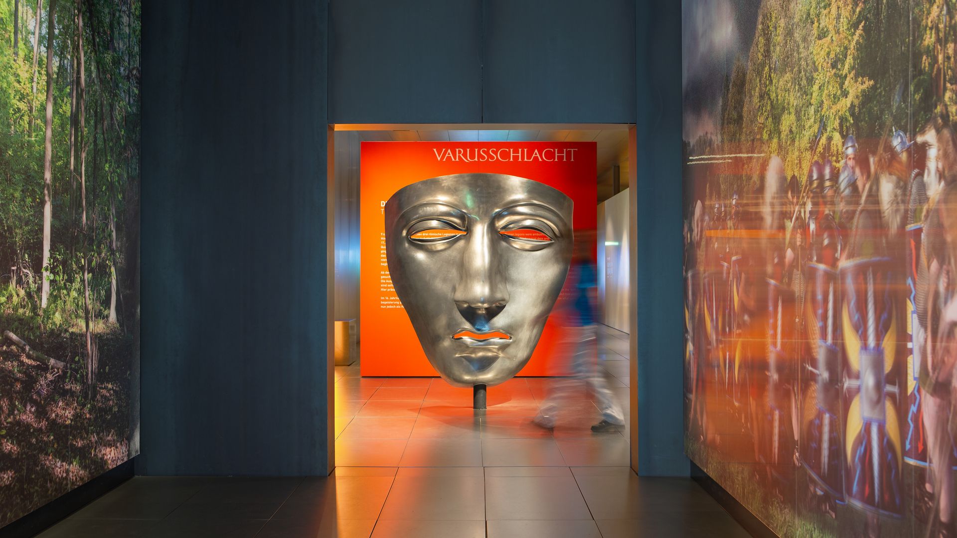 Große silberne Maske im Varusschlacht-Museum mit Besucher im Flur.
