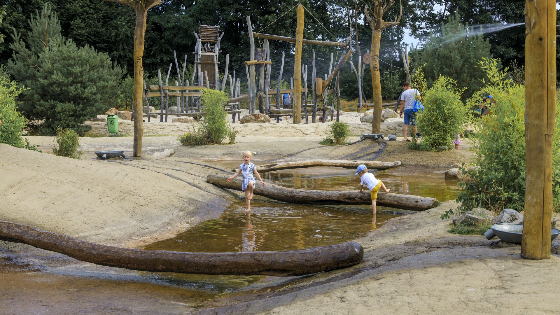 Kinderspielplatz mit Wasserspielbereich, Holzinstallationen und spielenden Kindern.