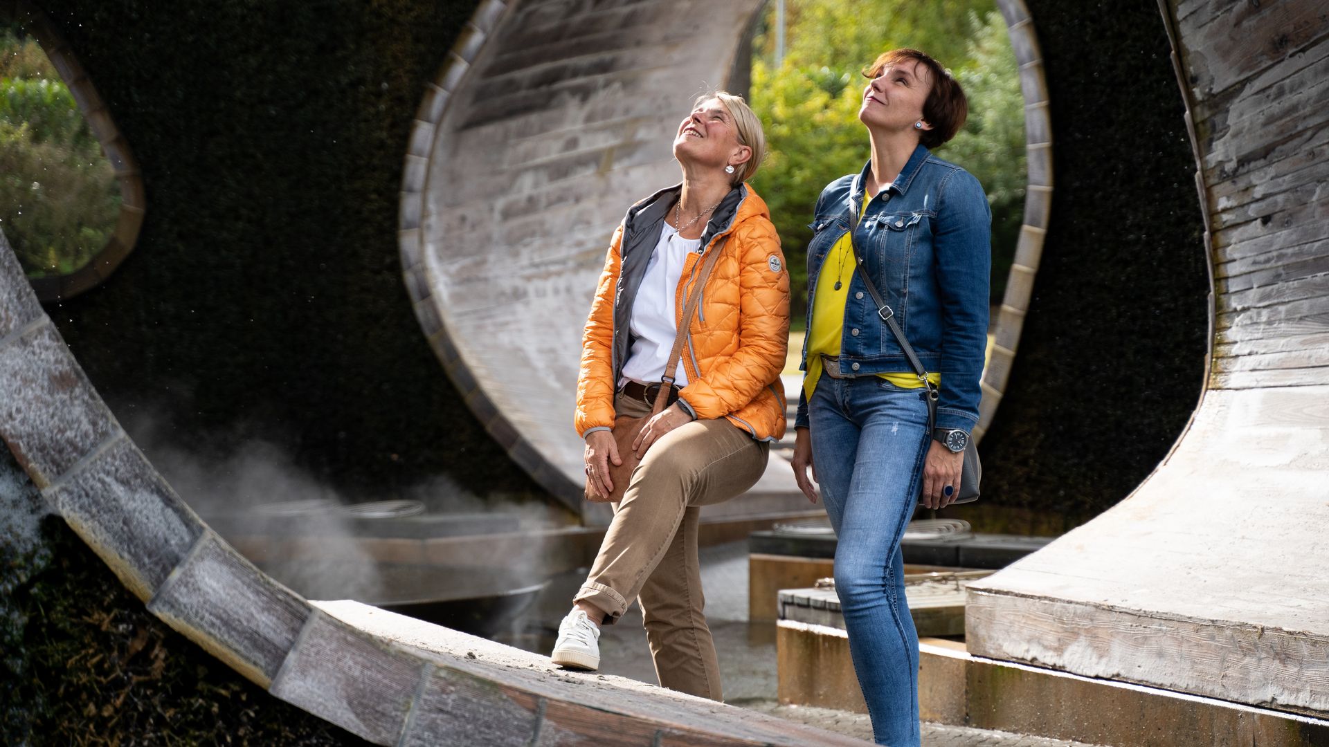 Zwei Frauen genießen eine künstlerische Skulptur im Freien bei sonnigem Wetter.