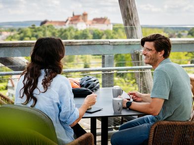 Bad Iburg Zwei Personen sitzen lächelnd an einem Tisch mit Blick auf eine Burg im Hintergrund.