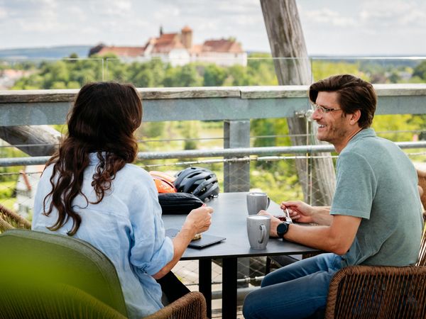 Bad Iburg Zwei Personen sitzen lächelnd an einem Tisch mit Blick auf eine Burg im Hintergrund.