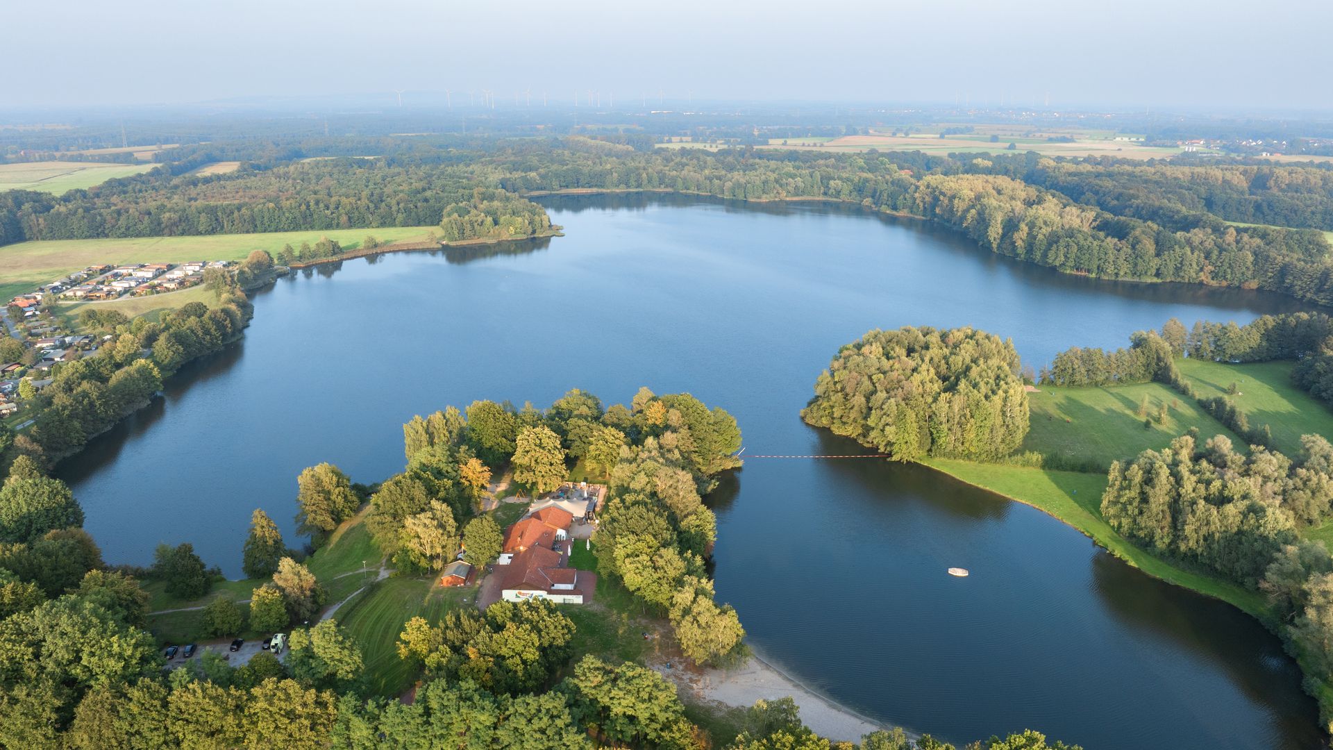 Luchtfoto van een meer met beboste oevers, een eiland en een klein stuk strand.