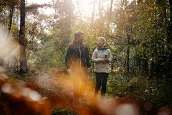 Zwei Personen wandern im sonnendurchfluteten Wald bei herbstlicher Stimmung.