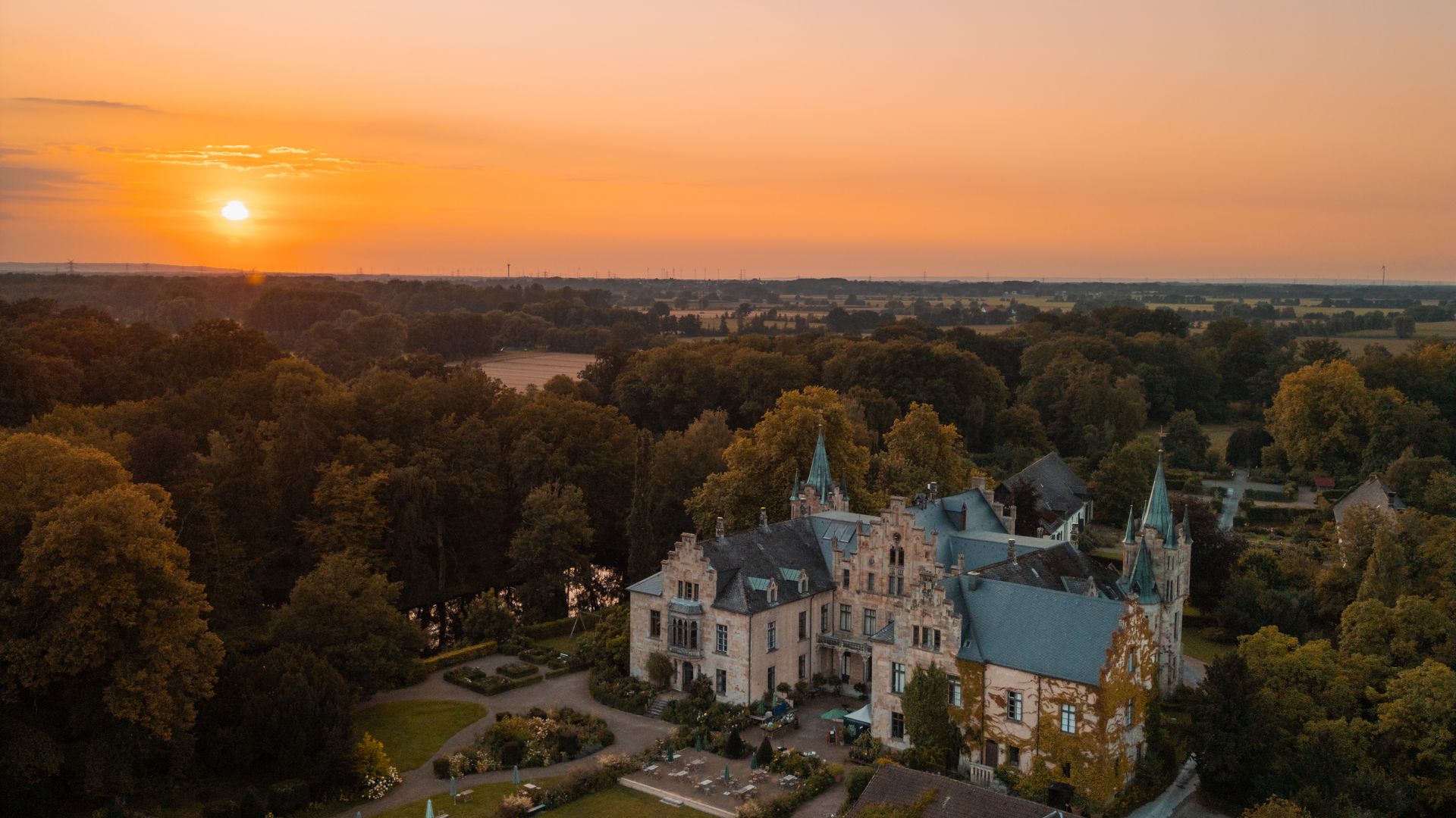 Schloss und Gartenlandschaft bei Sonnenuntergang im pastellfarbenen Abendhimmel.