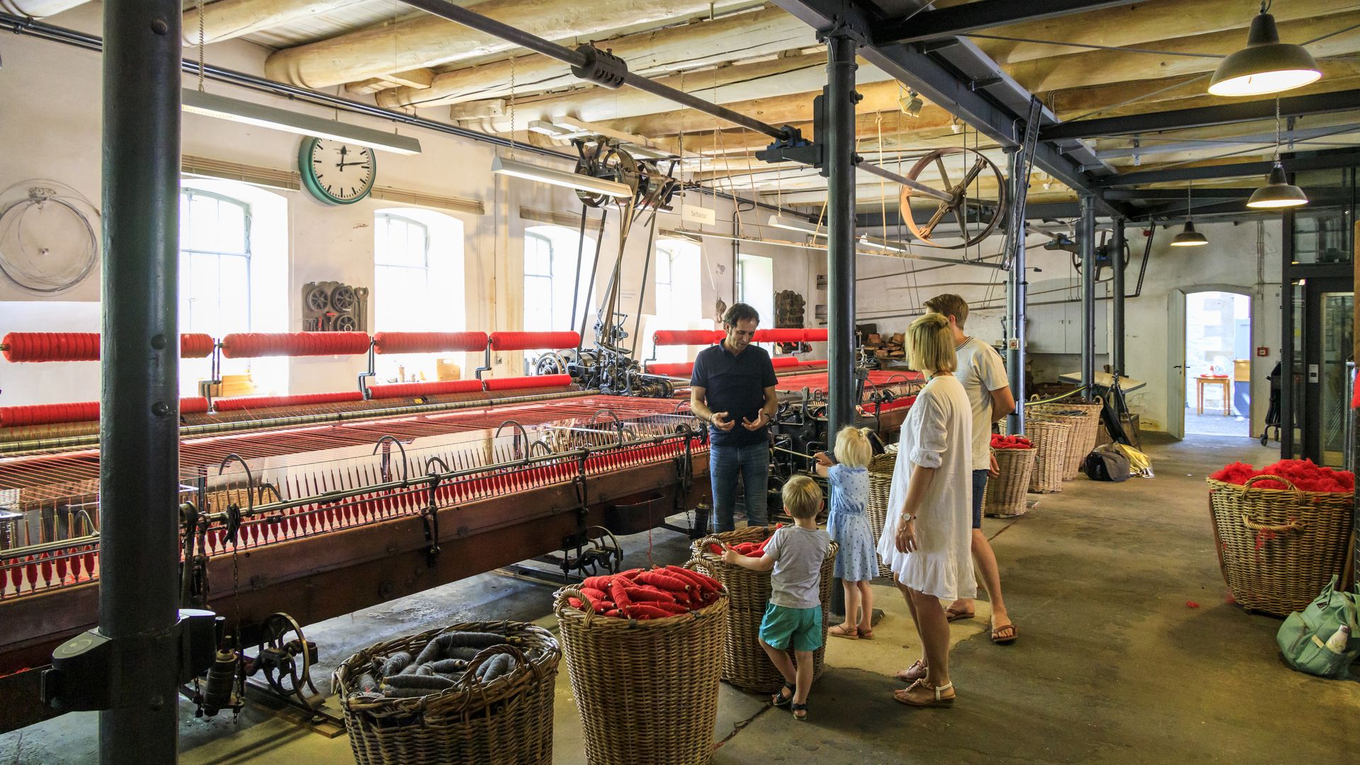 Innenansicht des Tuchmachermuseum Bramsche, mit historischen Webstühlen, Arbeitsmaterialien und Besucherinnen und Besuchern im Ausstellungsraum.