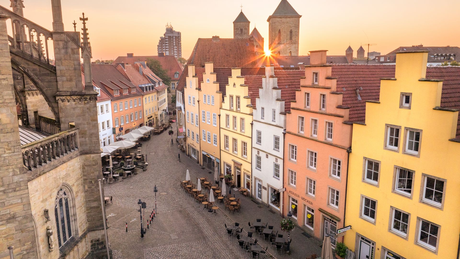 Historische Altstadthäuser bei Sonnenuntergang neben einer sonnendurchfluteten Kirche.