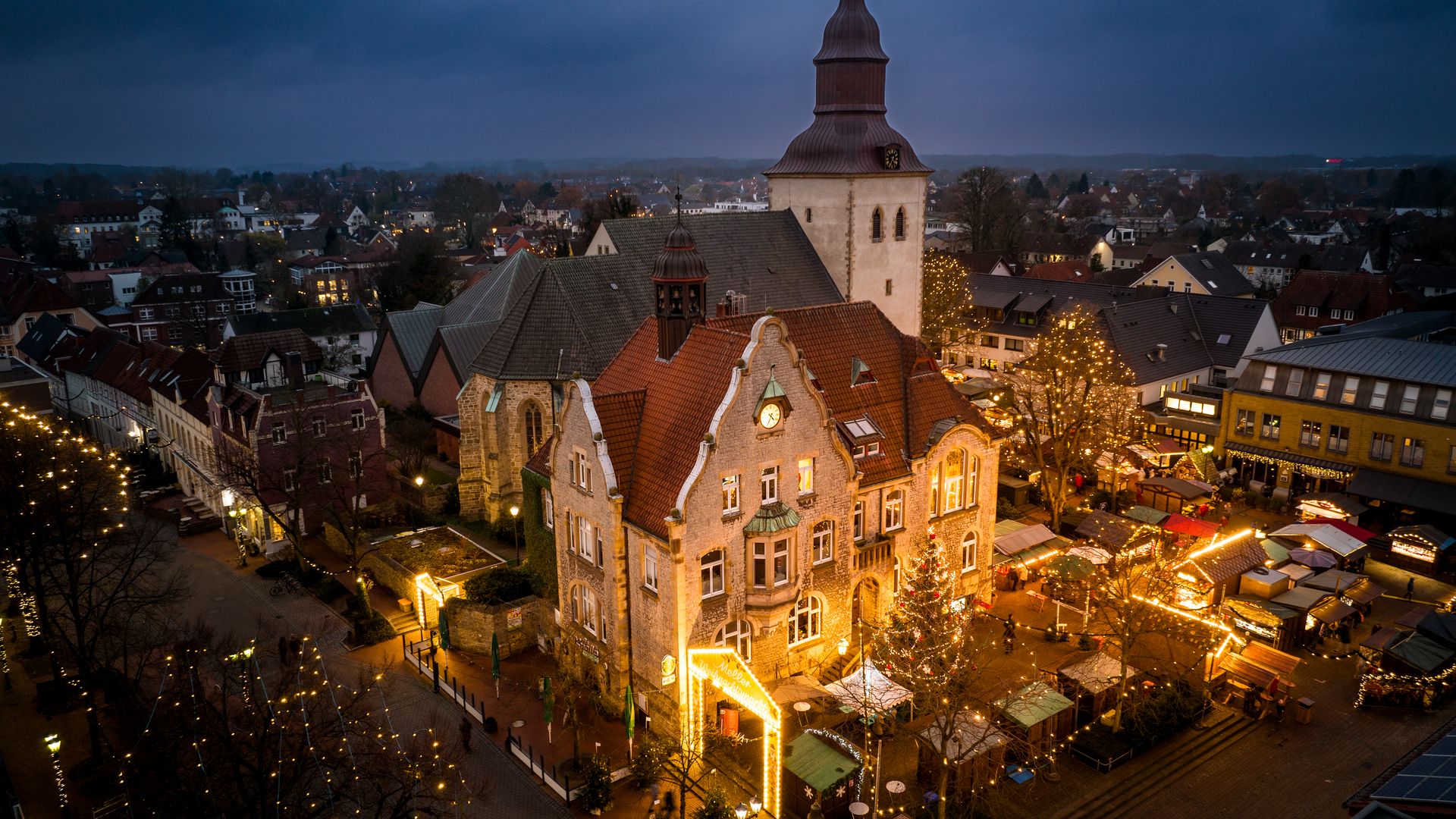 Abendliche Stadtansicht mit beleuchtetem Weihnachtsmarkt und historischer Kirche im Hintergrund.