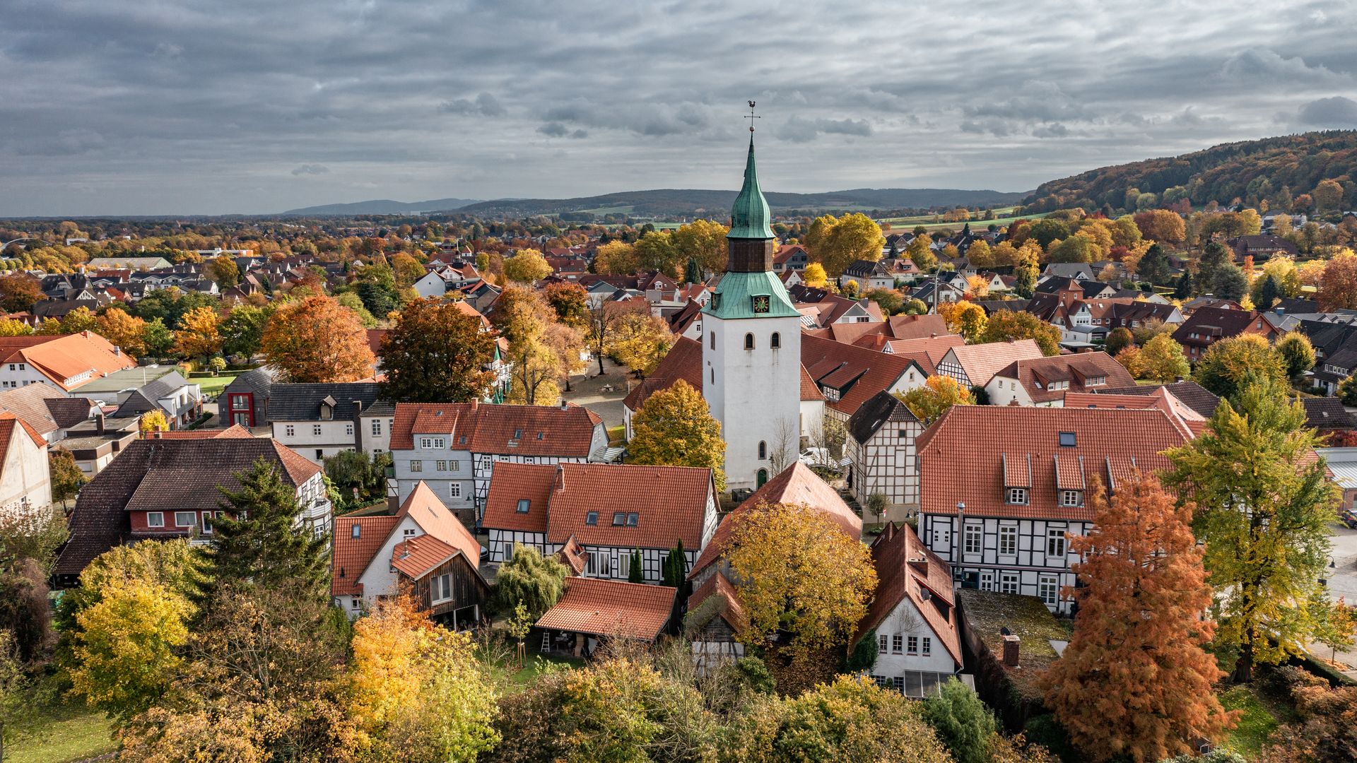 Luftaufnahme eines Dorfes mit historischem Kirchturm, Fachwerkhäusern und herbstlichem Laub.