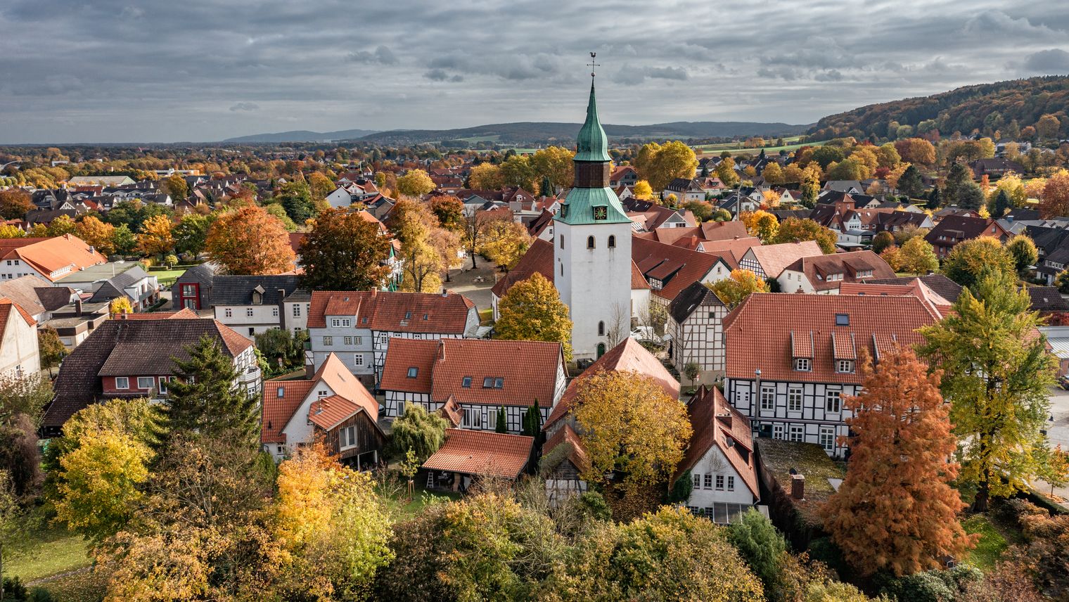 Luftaufnahme eines Dorfes mit historischem Kirchturm, Fachwerkhäusern und herbstlichem Laub.