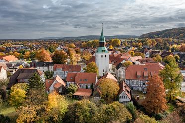 Luftaufnahme eines Dorfes mit historischem Kirchturm, Fachwerkhäusern und herbstlichem Laub.